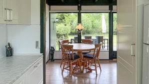 A dining area with a wooden table and chairs, a hanging light fixture, and a view of the outdoors.
