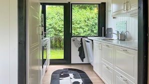 A narrow kitchen with a large window, a black and white rug, and a hanging towel.