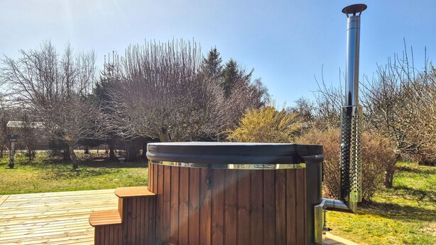 A hot tub on a wooden deck with a metal chimney, surrounded by trees.