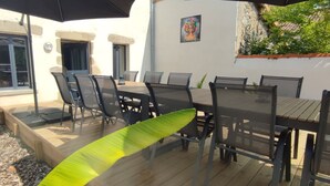 Un patio exterior con piso de madera, una mesa de comedor con sillas y dos sombrillas grandes que dan sombra.