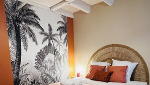 Habitación de hotel con cama, cabecero, pared con mural tropical y techo con vigas a la vista.