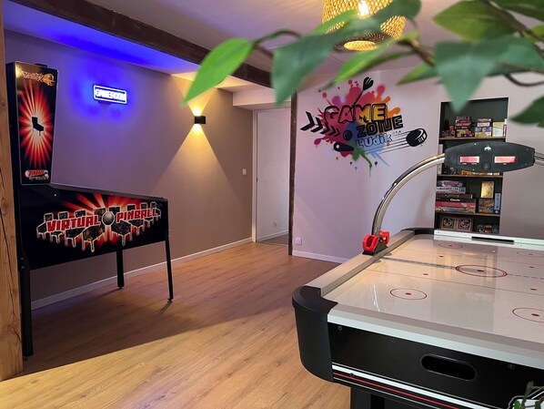 A room with a foosball table, a virtual pinball machine, and a bookshelf with board games.