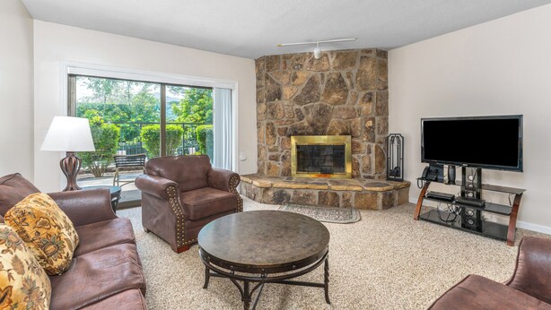 A living room with a stone fireplace, leather sofas, a round coffee table, and a TV on a stand. - Holly Ridge 102 | Cozy, Near Gatlinburg + Privacy (Gatlinburg)