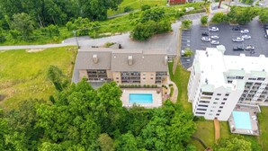 Vue aérienne d’un immeuble à plusieurs étages doté d’une piscine, d’un parking et entouré de verdure.
