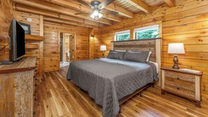A wooden cabin bedroom with a bed, nightstands, a ceiling fan, and a television. - Mountain Falls 14 | Family Friendly + Hot Tub (Sevierville)