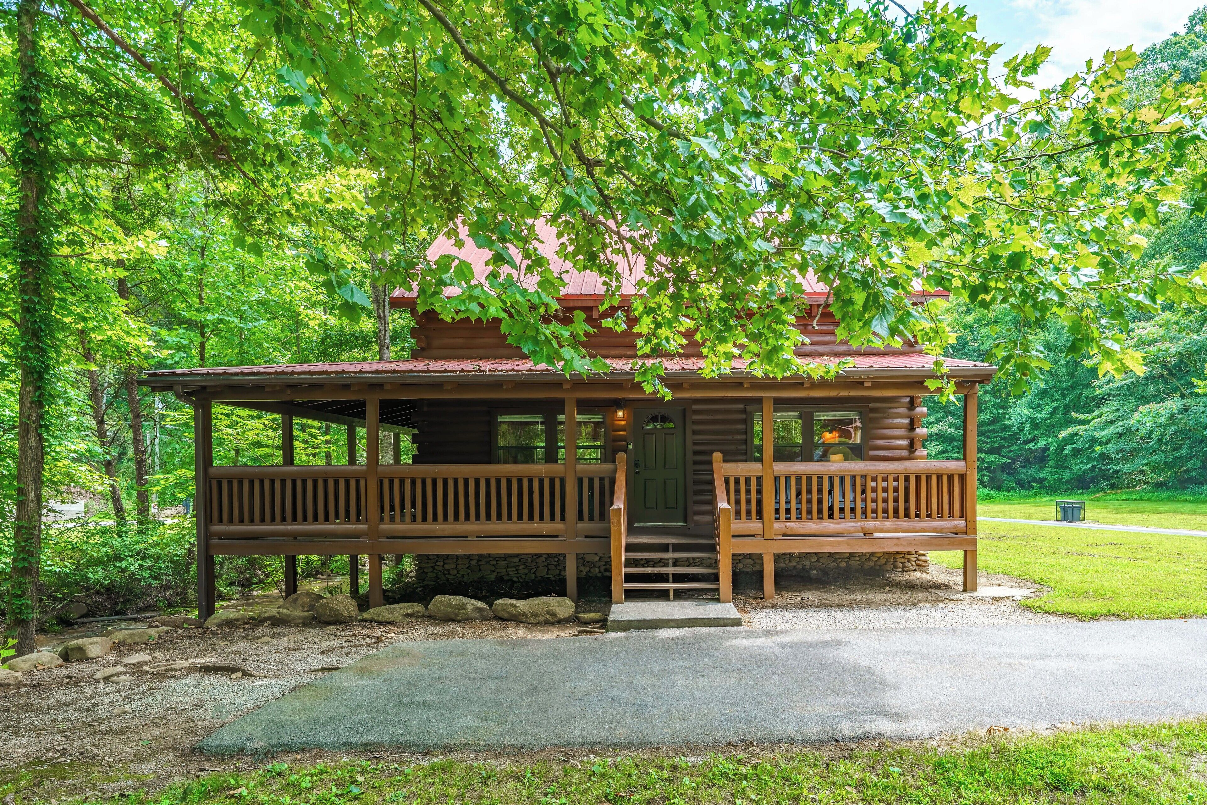 A wooden cabin with a porch, surrounded by trees and a stone wall.