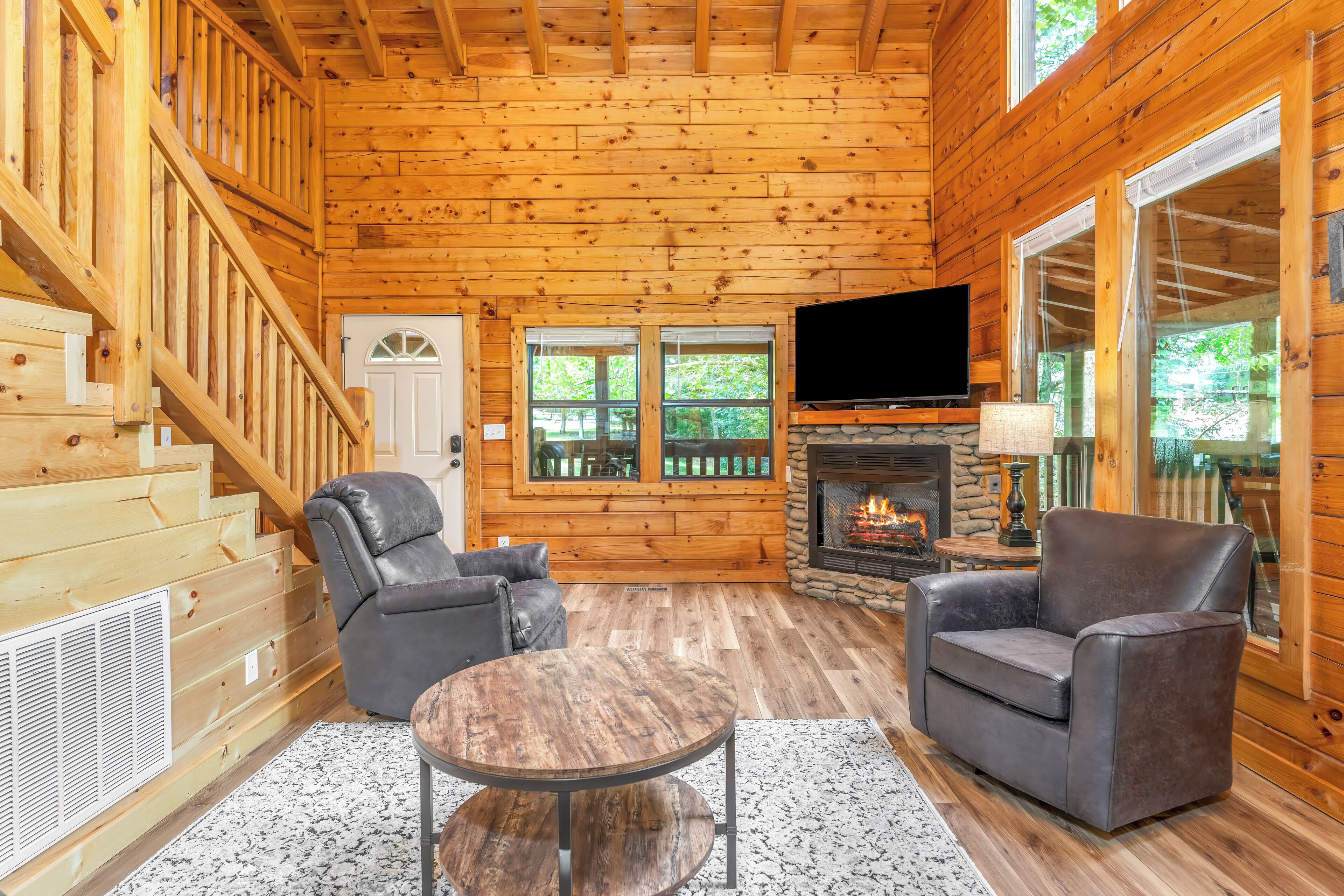 A log cabin interior with a fireplace, two leather sofas, a TV, and a stone fireplace surround.