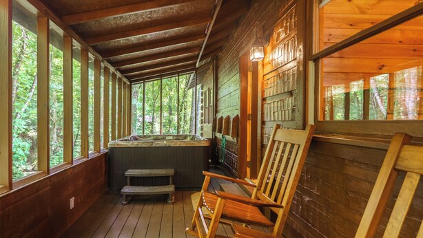 Una cabaña de madera con jacuzzi, sillas de madera y grandes ventanales con vistas a un bosque.