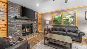 A living room with a stone fireplace, leather sofa, and a flat-screen TV mounted above the fireplace.
