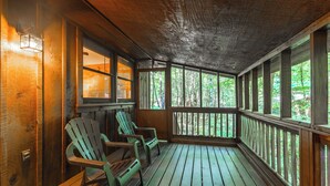 A wooden porch with two Adirondack chairs, a wooden ceiling, and large windows offering a view of trees.