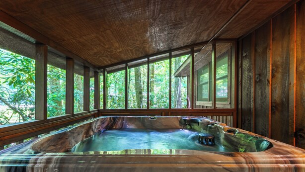 A hot tub in a wooden cabin with large windows and a view of the forest.