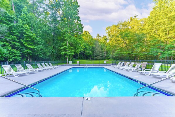 Une piscine rectangulaire dont la profondeur est indiquée par un repère à 3 pieds, entourée d’une terrasse en béton avec des chaises longues blanches et une rambarde en métal.