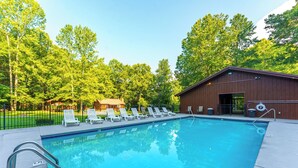 Une piscine avec des chaises longues, un bâtiment en bois et un espace clos planté d’arbres.