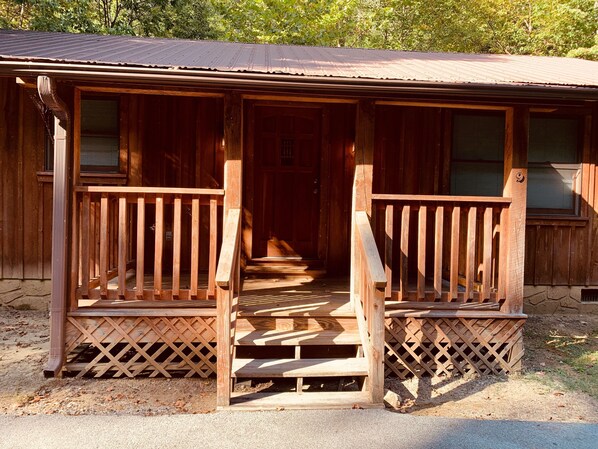 A wooden cabin with a porch, a staircase leading to the entrance, and a window with blinds.