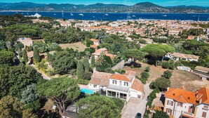 An aerial view of a coastal town with residential buildings, a swimming pool, and a marina with boats. - Family home 5 minutes walk from downtown! (Saint-Tropez)