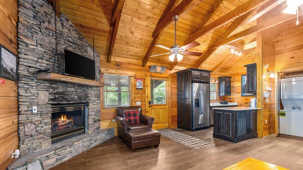 A log cabin interior with a stone fireplace, leather armchair, kitchen area, and wooden floors. - Little Bit of Heaven | Secluded + Woodland Haven (Sevierville)