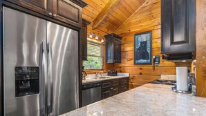 A modern kitchen with stainless steel appliances, wooden cabinetry, and a granite countertop. - Little Bit of Heaven | Secluded + Woodland Haven (Sevierville)