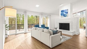 A modern living room with a white sofa, a fireplace, and a large window overlooking a deck.