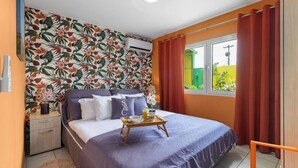 Une chambre à coucher avec un lit, une table de chevet, une fenêtre avec des rideaux et un papier peint à motifs floraux.