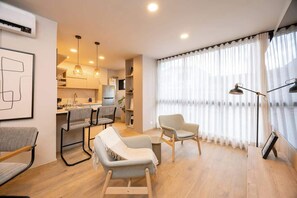 A modern living room with a dining area, a kitchen in the background, and a large window with sheer curtains. - Digital Nomad Paradise 2BR unit with A/C in Manila (Medellín)