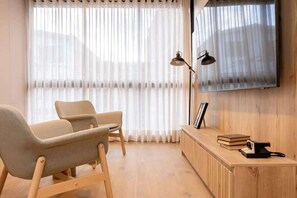 A modern living room with a sofa, a coffee table, a TV mounted on the wall, and a side table with books and a camera.