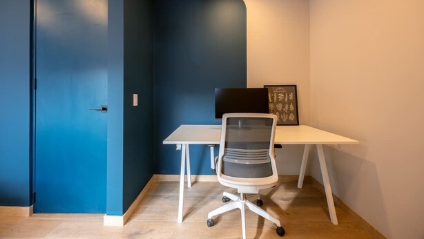 A room with a blue accent wall, a white desk, a modern office chair, and a framed picture on the wall.