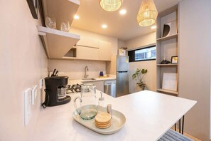 Een moderne keuken met een wit aanrecht, een koffiezetapparaat, een glazen karaf en een dienblad met stapels coasters.