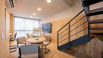 A modern living room with a round table, chairs, a TV mounted on the wall, and a wooden staircase.