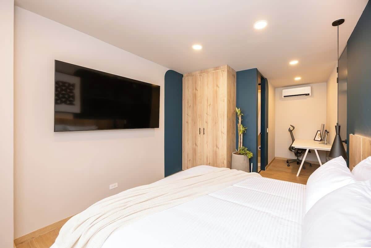 Une chambre moderne avec un grand lit, un téléviseur fixé au mur, un bureau avec une chaise et un appareil de climatisation.