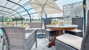 A covered outdoor seating area with wicker furniture, a round table, and a large umbrella. - Charmante Maison avec piscine (Lacropte)