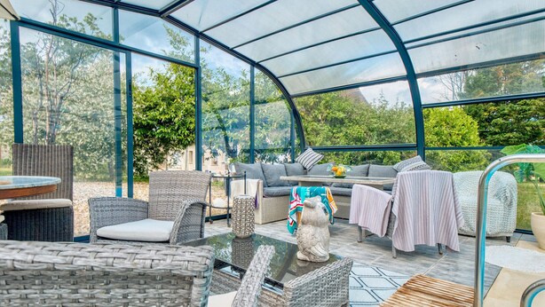 A greenhouse with wicker furniture, a glass table, and a stone sculpture. - Charmante Maison avec piscine (Lacropte)