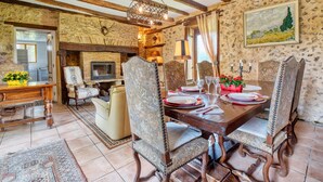 A rustic dining room with a wooden table set for four, surrounded by upholstered chairs. A fireplace is visible in the background, and a painting adorns the wall. - Charmante Maison avec piscine (Lacropte)