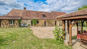 A rustic stone house with a tiled roof, a wooden pergola, and a gravel courtyard. - Charmante Maison avec piscine (Lacropte)