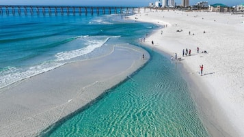 Une plage à l’eau turquoise et limpide, une jetée qui s’avance dans l’océan et des bâtiments en arrière-plan.