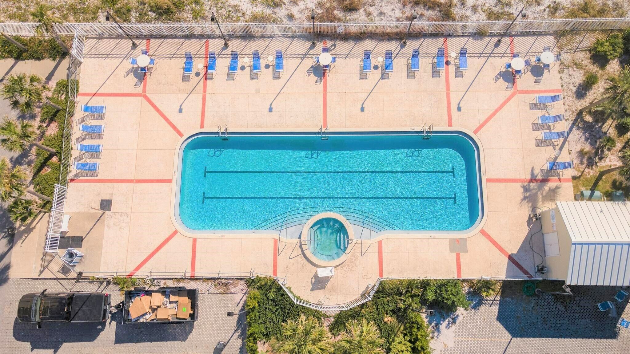 Vue aérienne d’une piscine dotée de plusieurs couloirs, entourée de chaises longues et d’un espace de repos abrité.