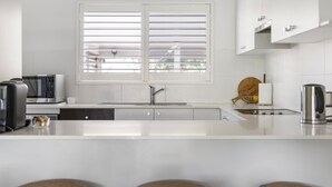 Een moderne keuken met een wit aanrecht, een spoelbak, een magnetron en een waterkoker.