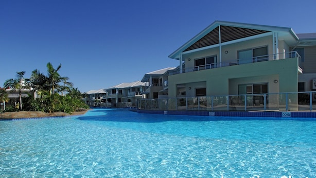 Een resort met een groot zwembad, meerlaags gebouwen en palmbomen.