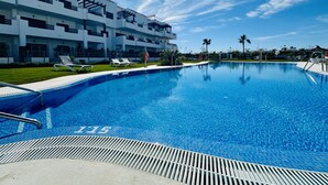Un hôtel moderne doté d’une piscine, de chaises longues et offrant une vue sur un ciel d’un bleu éclatant.