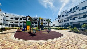 Une aire de jeux dotée d’équipements colorés, entourée d’une zone pavée avec des carreaux décoratifs.