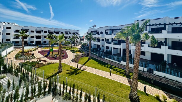 Un ensemble immobilier moderne composé de plusieurs bâtiments, doté d’une cour intérieure avec des palmiers et d’une aire de jeux.