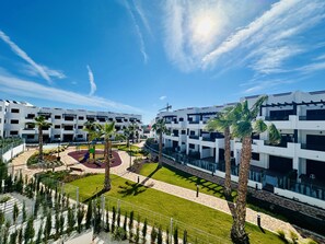 A modern building complex with multiple floors, a central courtyard with palm trees, and a playground. - Apartamento Melya (Mar de Pulpi) (San Juan de los terreros)