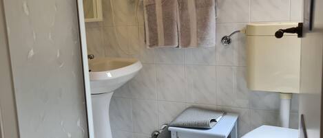 A bathroom with a toilet, sink, and a small stool with a towel.