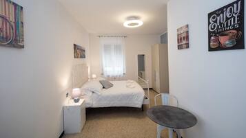 A bedroom with a bed, bedside table, chair, and a painting on the wall.
