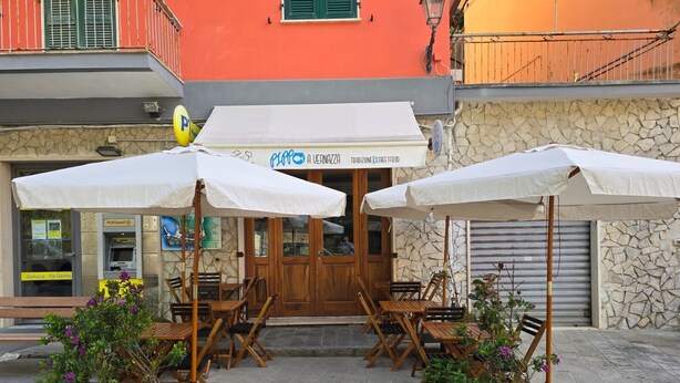 An outdoor seating area with wooden tables and white umbrellas, in front of a building with a stone facade and a sign reading "A Vernazza Tradizione & Street Food". - Pippo a vernazza rooms (Vernazza)