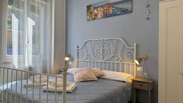 Un dormitorio con cama, una mesita de noche, una lámpara de pared, un cuadro y una ventana con cortinas.