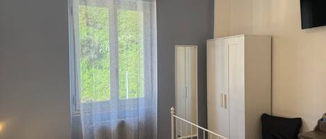 A bedroom with a bed, a wardrobe, a desk, and a window with curtains.