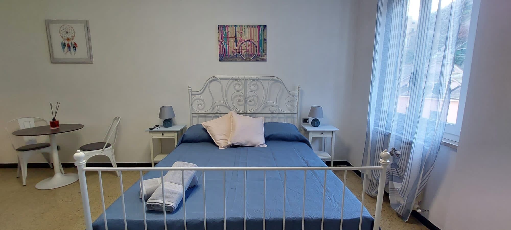 A bedroom with a bed, two bedside tables, a chair, a small table, and a window with curtains.