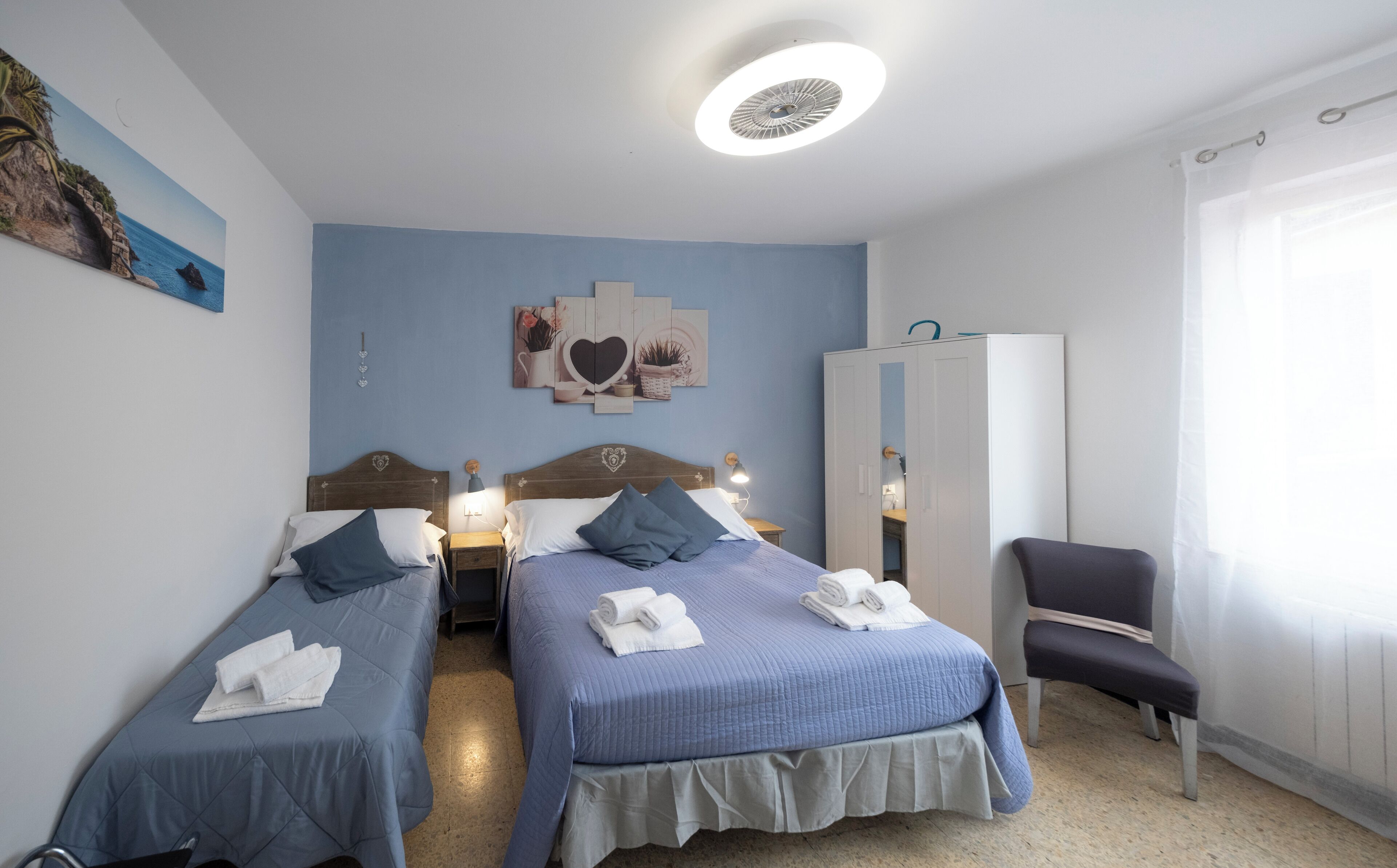 Habitación de hotel con dos camas, un armario, una silla y una lámpara en el techo.