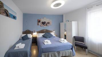Habitación de hotel con dos camas, un armario, una silla y una lámpara en el techo.