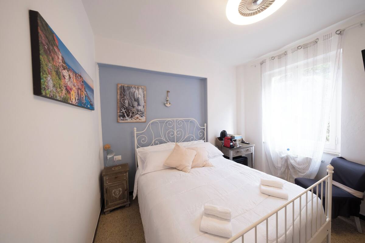 Une chambre à coucher avec un lit, une table de chevet, une chaise, un bureau et une fenêtre avec des rideaux.
